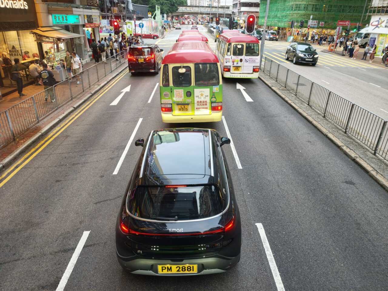 高位俯影行駛中的 Smart 車與小巴,車牌同路面標線仍清晰,動態定格夠穩