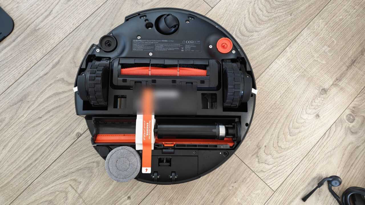 Xiaomi 掃拖機器人 6 Max - 裏返した機体：上方には絡まり防止主ブラシ、下方にはローラーのモッピングエリア、左下角には伸縮可能な角落ちモップがあります（機体のバーコードは隠されています）。