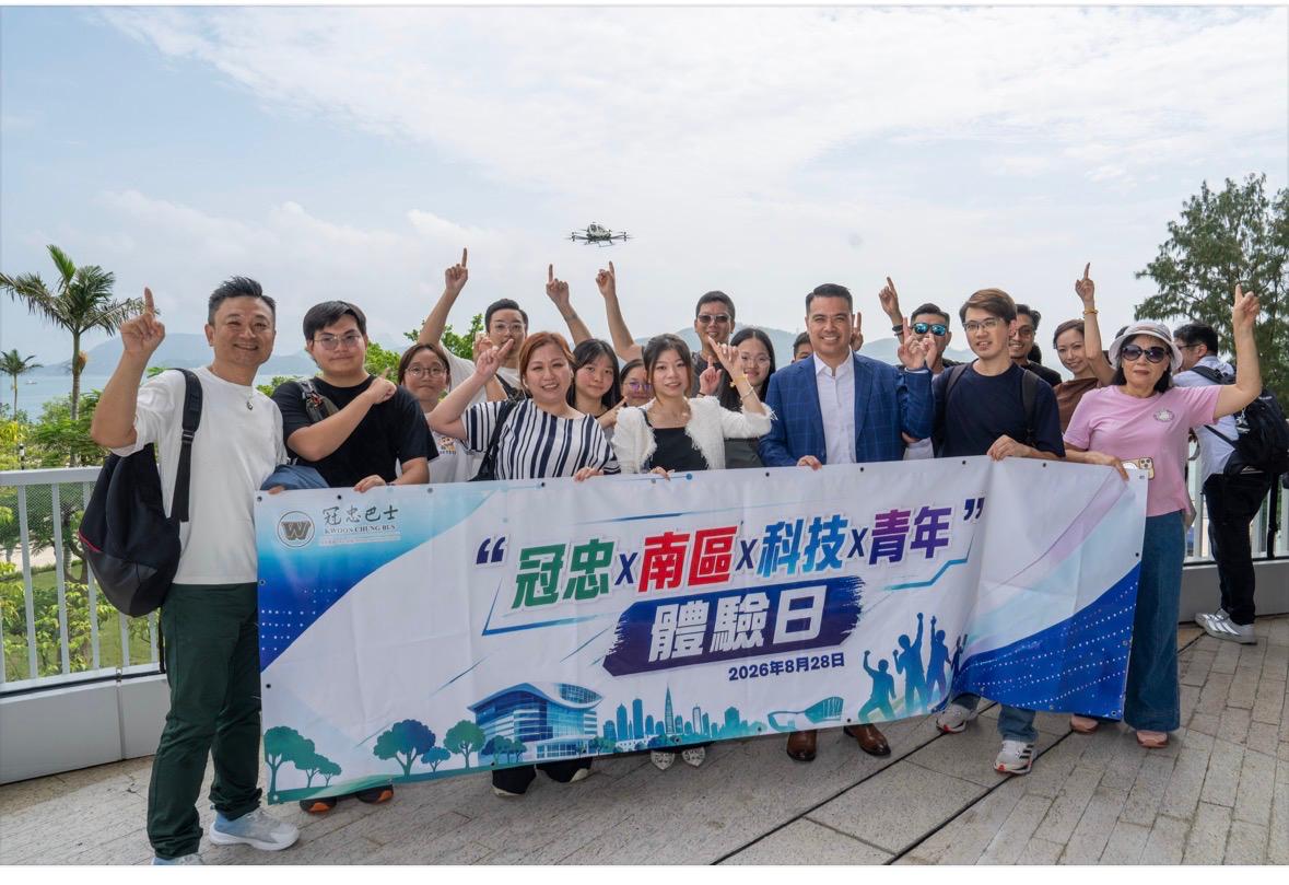 Junge Menschen aus dem Süden Hongkongs heben ein Banner für den Erfahrungstag mit dem GMB Smart Mobility Team am Hafen von Cyberport, während EH216-S am Himmel vorbeifliegt.