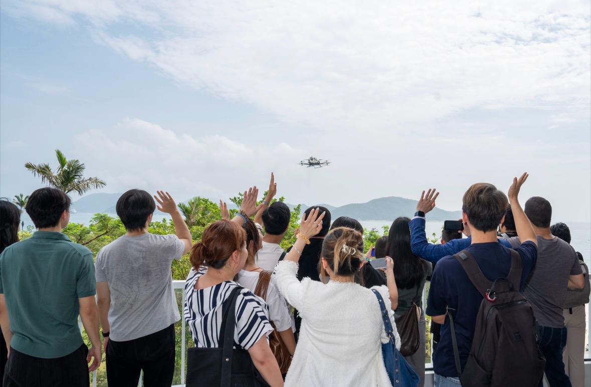 Junge Menschen aus dem Süden Hongkongs heben die Hände in die Luft, während EH216-S über dem Hafen von Cyberport fliegt.